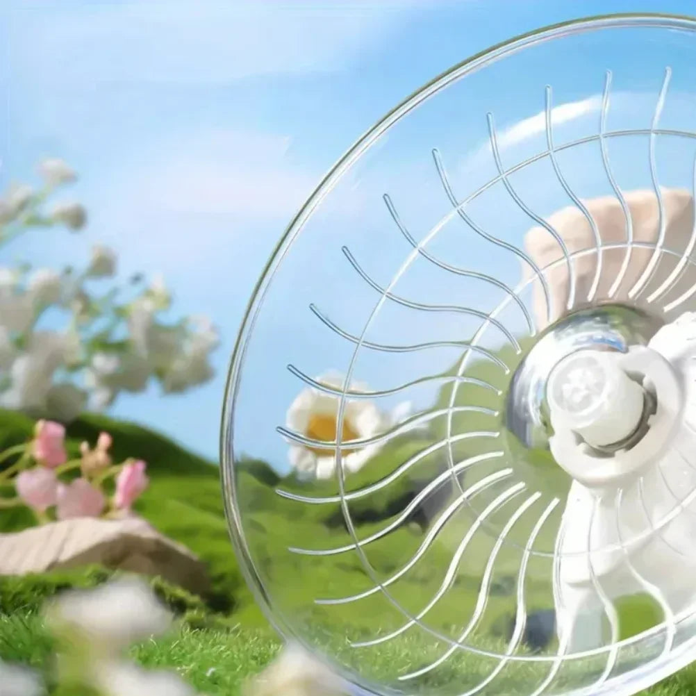 Nahaufnahme einer stillen, transparenten Laufrolle für kleine Haustiere, umgeben von grünem Gras und weißen Blumen.