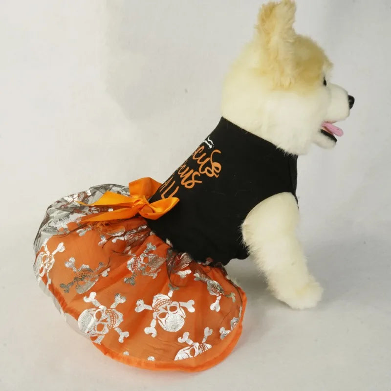 A white dog wearing a black dress with an orange ruffled skirt decorated with skulls and a bow.