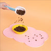 A hand is pouring dark pet food onto a pink silicone feeding mat for dogs and cats.