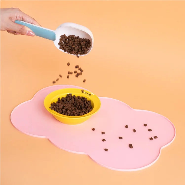 A hand is pouring dark pet food onto a pink silicone feeding mat for dogs and cats.