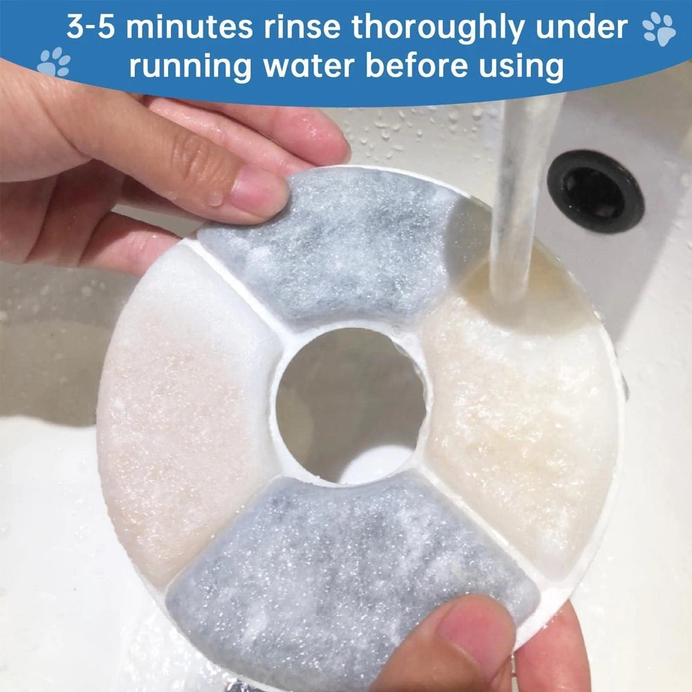Eine Hand spült einen Filterspender einer Haustierbrunnenanlage unter fließendem Wasser.