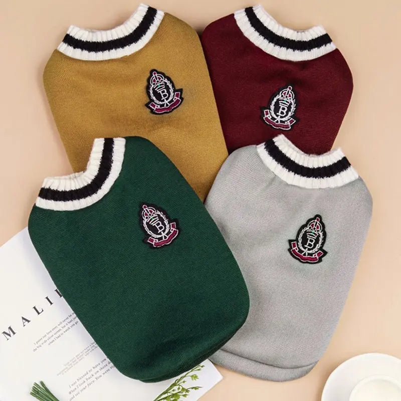 Three knitted vests for small dogs in mustard yellow, burgundy, and forest green with embroidered emblems.