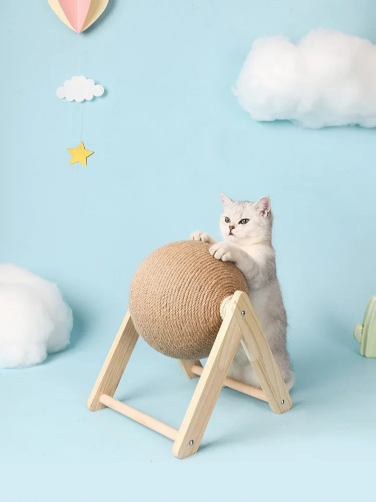 A fluffy gray kitten is interacting with a round sisal rope ball toy supported by a wooden base against a light blue backgrou