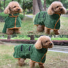 Un chien brun clair et duveteux portant un manteau de serviette vert foncé avec des bordures orange.