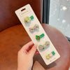 A hand holds a pack of five handmade flower-shaped baby hair clips in various shades of green and pink on a white card.