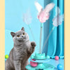 A gray cat sits next to a colorful interactive toy featuring a turntable, rolling balls, and feather wands.
