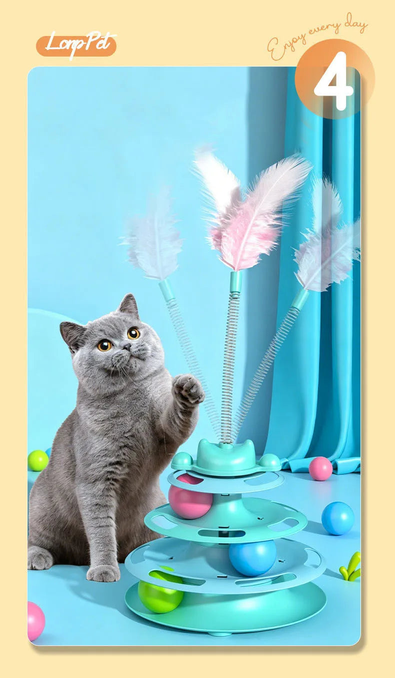 A gray cat sits next to a colorful interactive toy featuring a turntable, rolling balls, and feather wands.