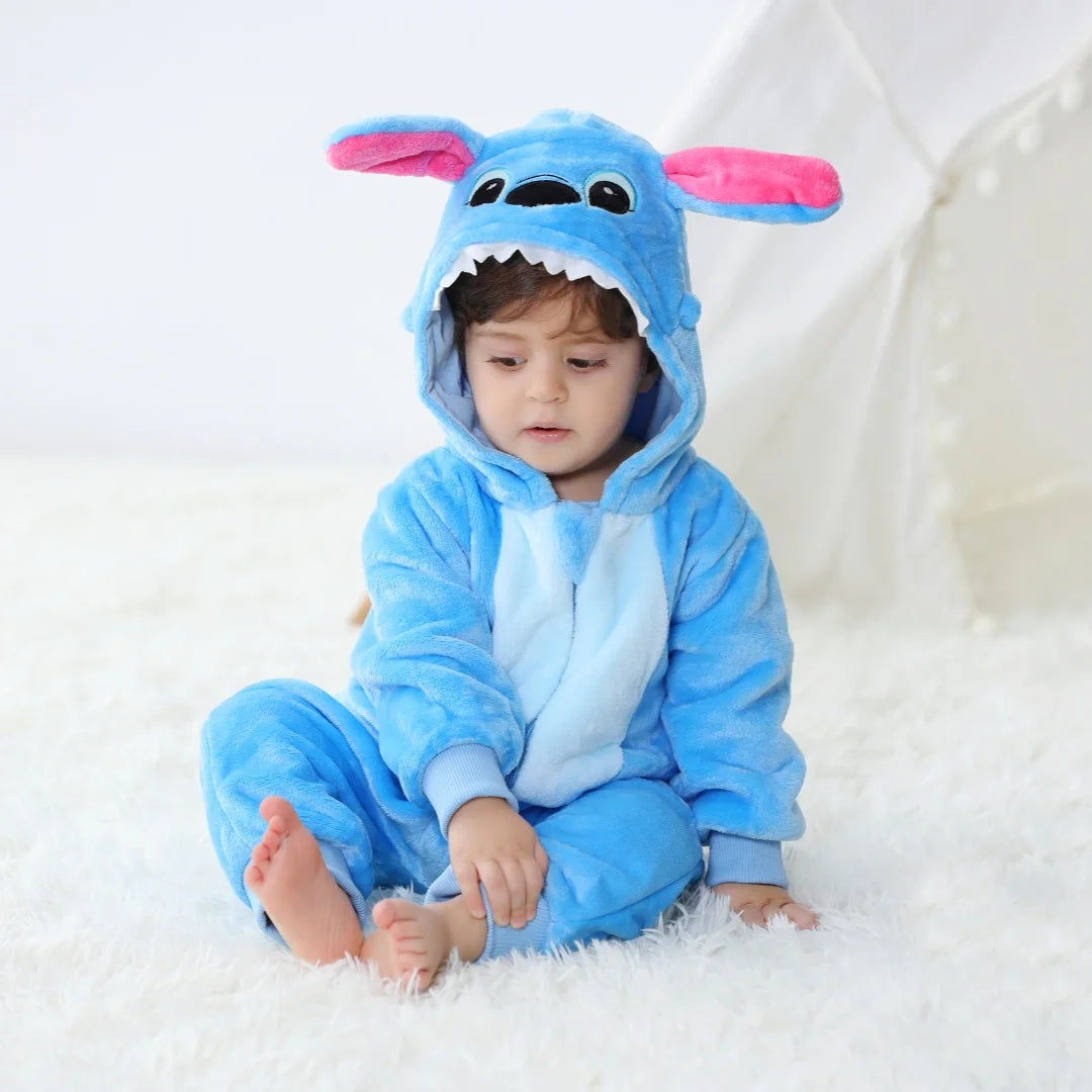 A baby wearing a blue cartoon animal hooded romper with pink ears sitting on a white surface.