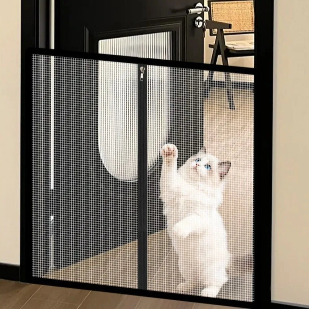 A white kitten is visible through a black metal mesh pet gate and barrier.