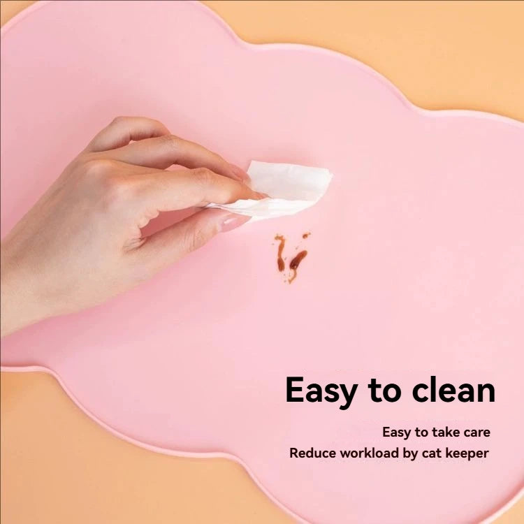 A hand is placing a piece of tissue on a pink silicone pet feeding mat, demonstrating its easy to clean feature.