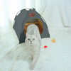 A fluffy gray cat is looking out of a dark gray foldable pet tent on a white, furry surface.