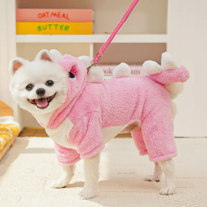 A white dog wearing a pink fleece hoodie with animal ears standing on a light rug.