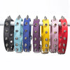 A row of colorful studded leather dog collars with metal rivets displayed on a white rod.