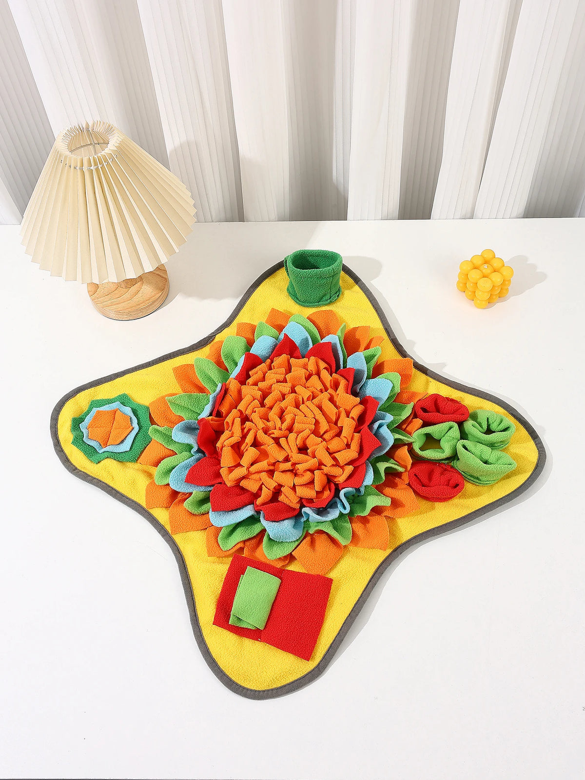 A colorful, textured snuffle mat for dogs with various fabric pieces arranged in a flower shape.