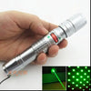A hand holds a silver laser pointer with a green beam, demonstrating its use for cats or outdoor purposes.