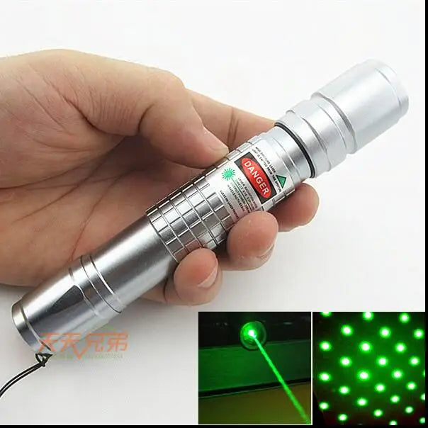 A hand holds a silver laser pointer with a green beam, demonstrating its use for cats or outdoor purposes.