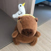A brown capybara plush toy with a white, yellow-tipped wing attached.