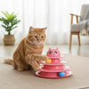An orange tabby cat is interacting with a pink 3-layer cat turntable toy featuring colorful balls.