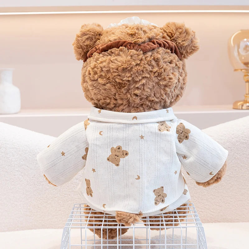 A brown teddy bear plush wearing a white pajama top with gold star and animal embroidery.