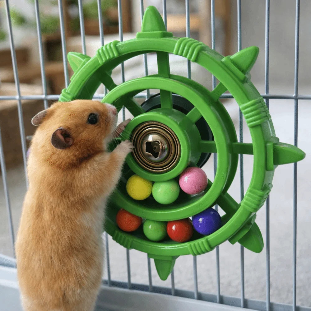 A brown hamster is interacting with a green parrot spinner rattle toy inside a cage.