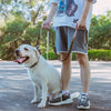 A person holds a heavy-duty tactical dog leash with dual handles and bungee attached to a white dog outdoors.
