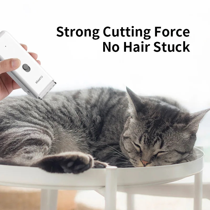 Eine Katze ruht auf einer weißen Fläche, während eine Hand einen weißen Pflege-Trimmer in der Nähe ihres Fells hält.