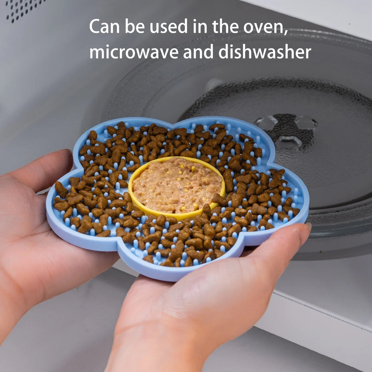 A hand holds a silicone lick mat filled with dog food, demonstrating its use in an oven, microwave, and dishwasher.