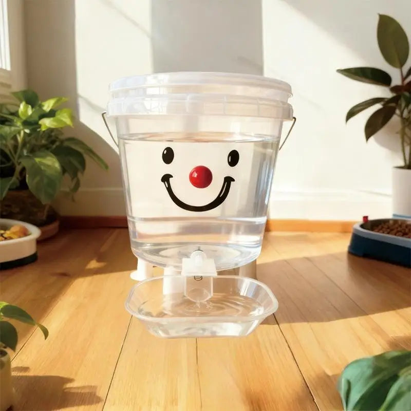 A clear plastic cartoon gravity pet water dispenser with a smiling face sits on a wooden floor.