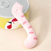 A pink silicone pet can opener and feeding spoon with a sealing lid resting on a yellow tin.