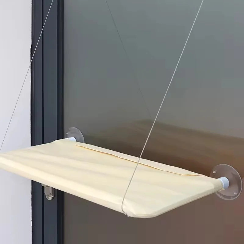 A beige hammock bed suspended by thin cords and suction cups, designed for a cat window.