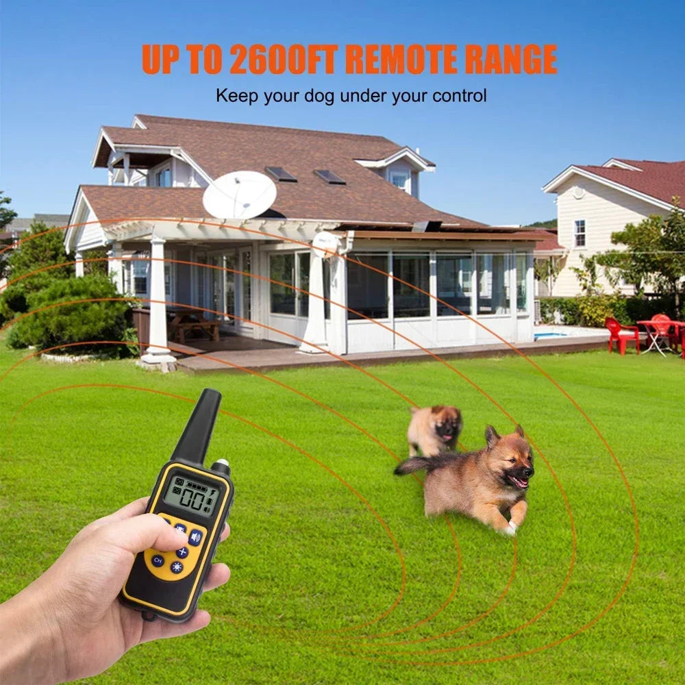 A hand holds a remote dog training collar with an LCD display, demonstrating its up to 2600ft remote range over a grassy yard