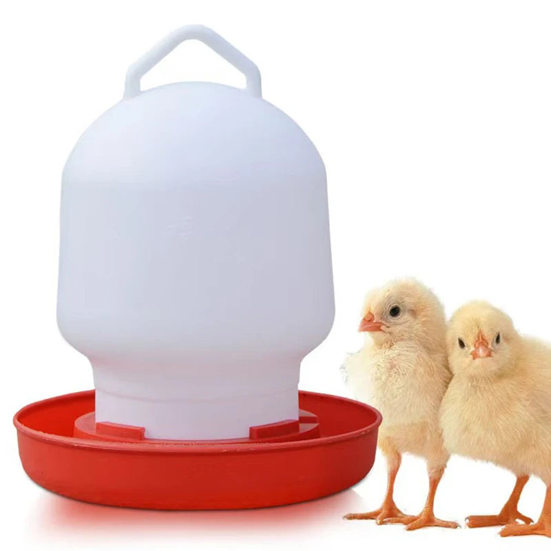 A white automatic poultry feeder and waterer sits on a red tray with two yellow chicks.