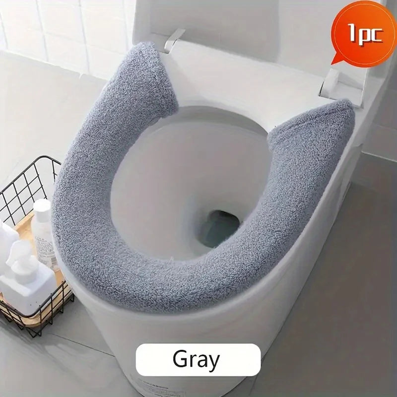 A gray plush non-slip toilet seat cover is shown installed on a white toilet bowl.
