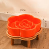 An orange ceramic slow feeder cat bowl rests on a natural wooden stand.