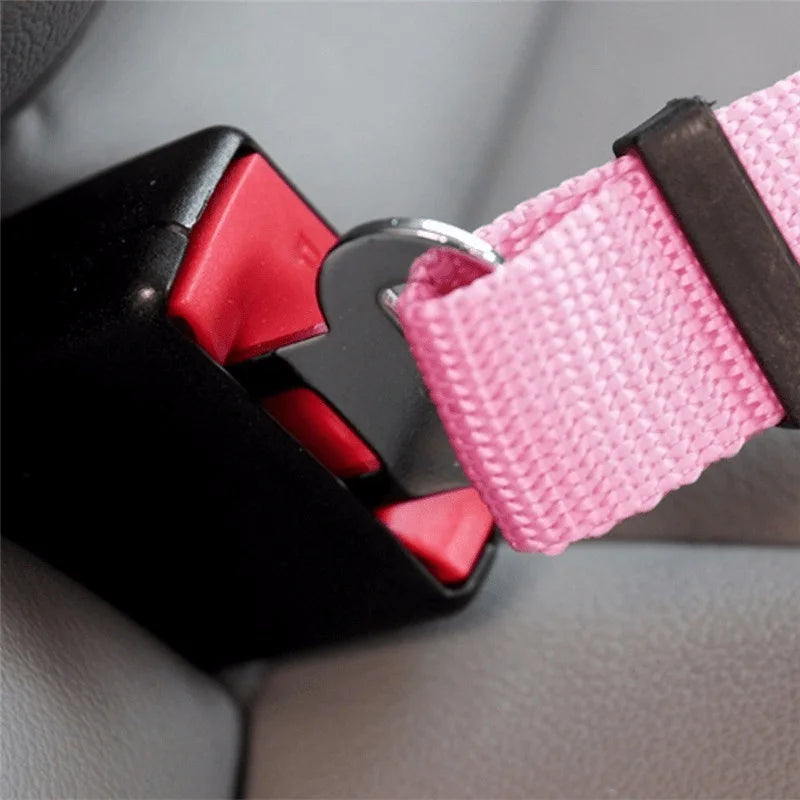 A close-up of a black headrest restraint with a pink nylon strap and silver buckle for a dog car seatbelt tether.