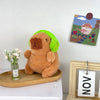 A brown capybara plush toy wearing a lime green hood sitting next to a framed illustration.