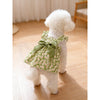 A fluffy white dog wearing a green floral patterned summer dress with a matching green bow.