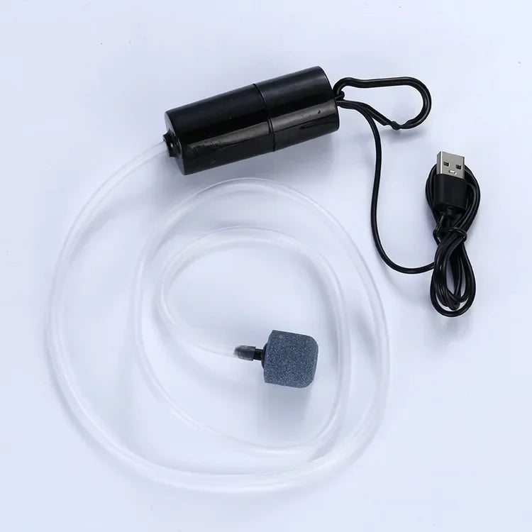 A black portable USB aquarium air pump with a clear tube and a small gray accessory is shown on a white background.