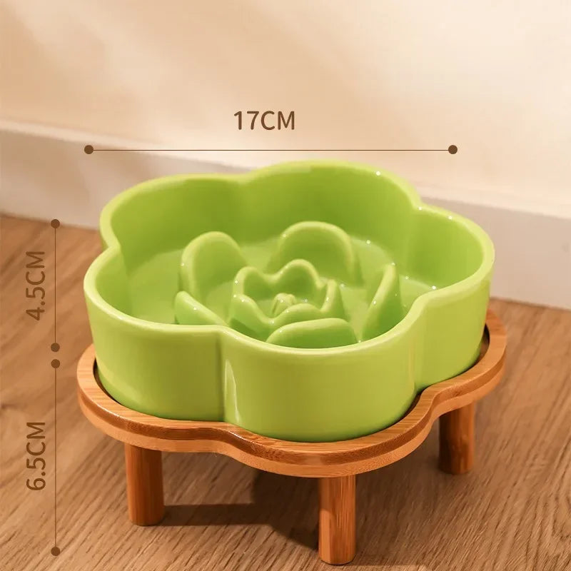 A lime green ceramic slow feeder cat bowl rests on a natural wooden stand.