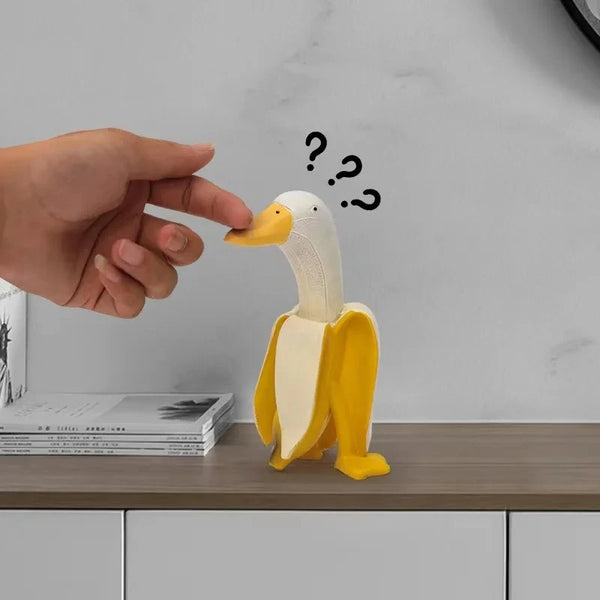 Gelbe Harf-Banane-Enten-Gartenskulptur neben einer Hand mit Fragezeichen auf Holzoberfläche.