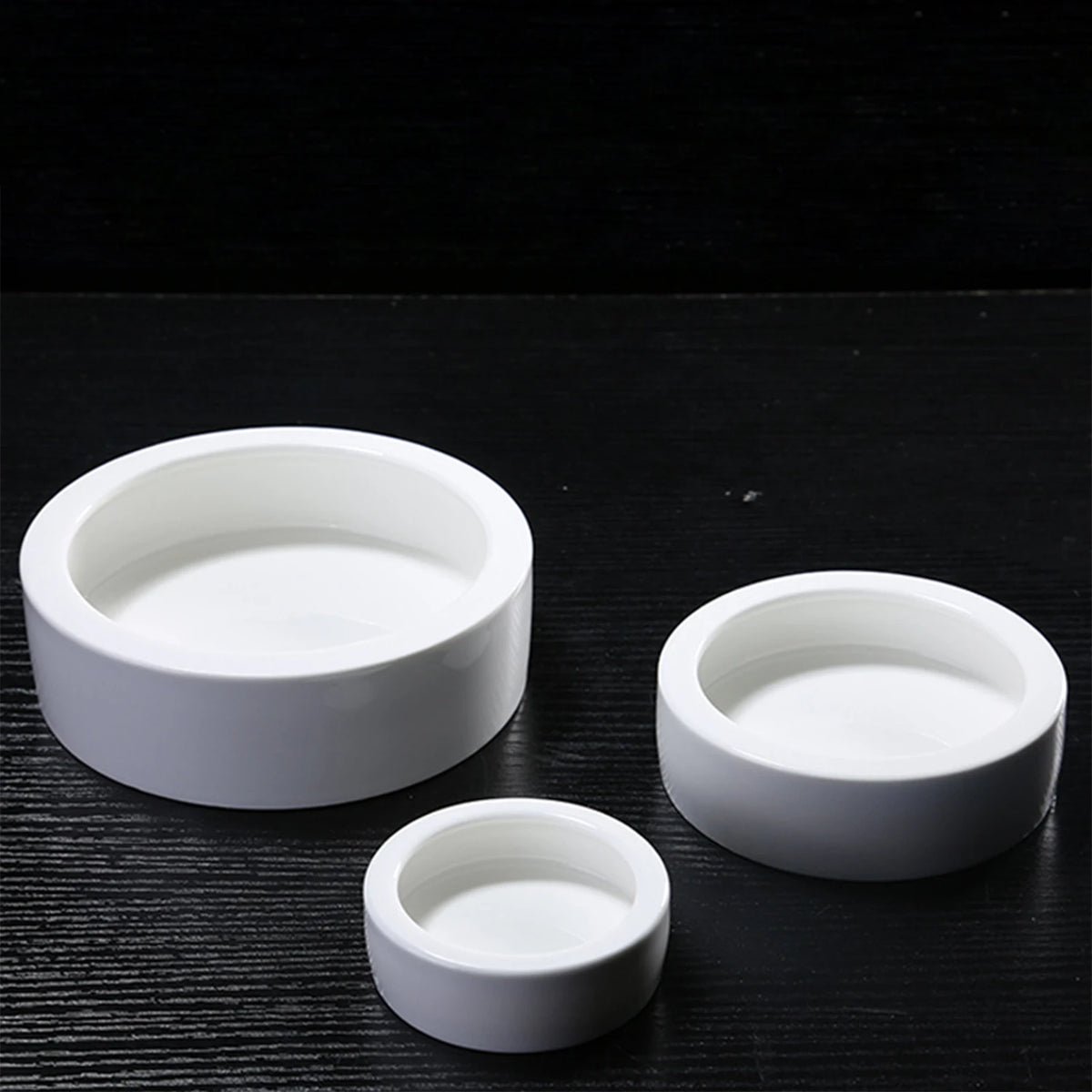 A set of three white ceramic reptile feeding and watering bowls placed on a dark surface.