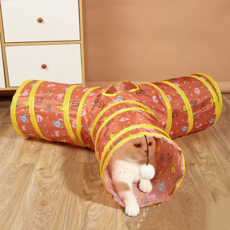 Orangefargenes und gelbes zusammenfaltbares Katzentunnel, benutzt von einer kleinen weißen Katze.