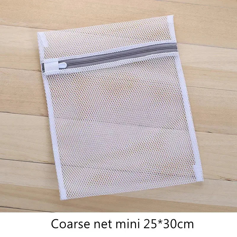 Una bolsa de ropa de malla transparente con cremallera gris sobre una superficie de madera.