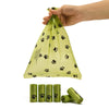 A hand is holding a clear biodegradable pet poop bag with black paw prints, next to several rolls of the same bags.