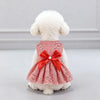 Ein weißer Pudel trägt ein rot-weiß kariertes Sommerkleid mit einer großen roten Schleife.