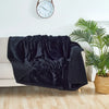 A dark black fluffy microfiber blanket draped over a white sofa next to a potted green plant.