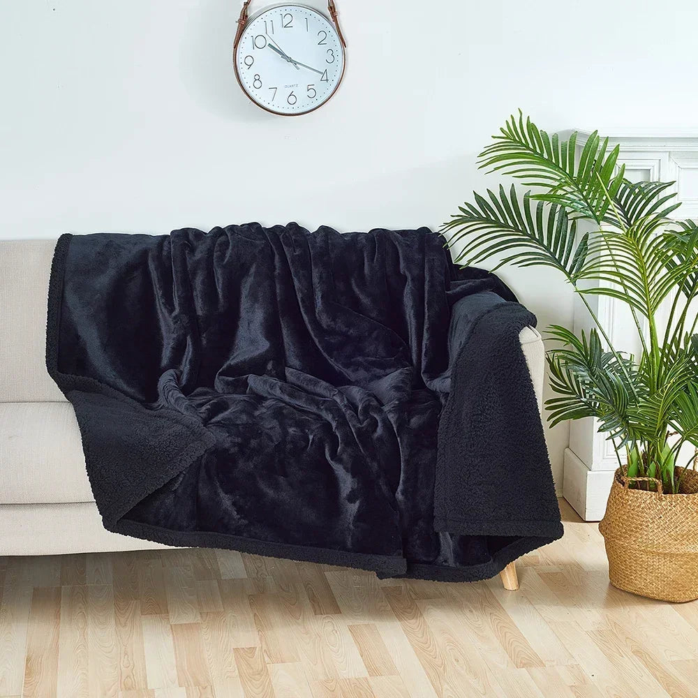 A dark black fluffy microfiber blanket draped over a white sofa next to a potted green plant.