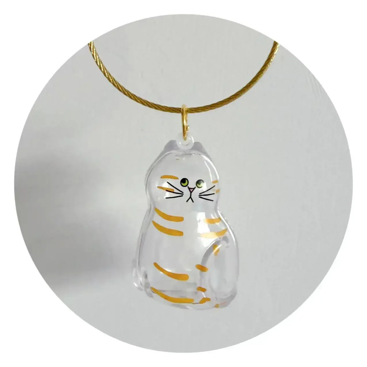 A clear glass charm shaped like a cat with striped markings suspended from a gold-colored cord.
