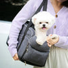A woman holds a gray portable pet car seat with a white dog sitting on top of it.