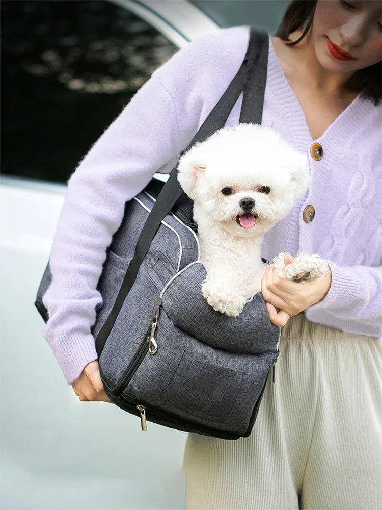 A woman holds a gray portable pet car seat with a white dog sitting on top of it.
